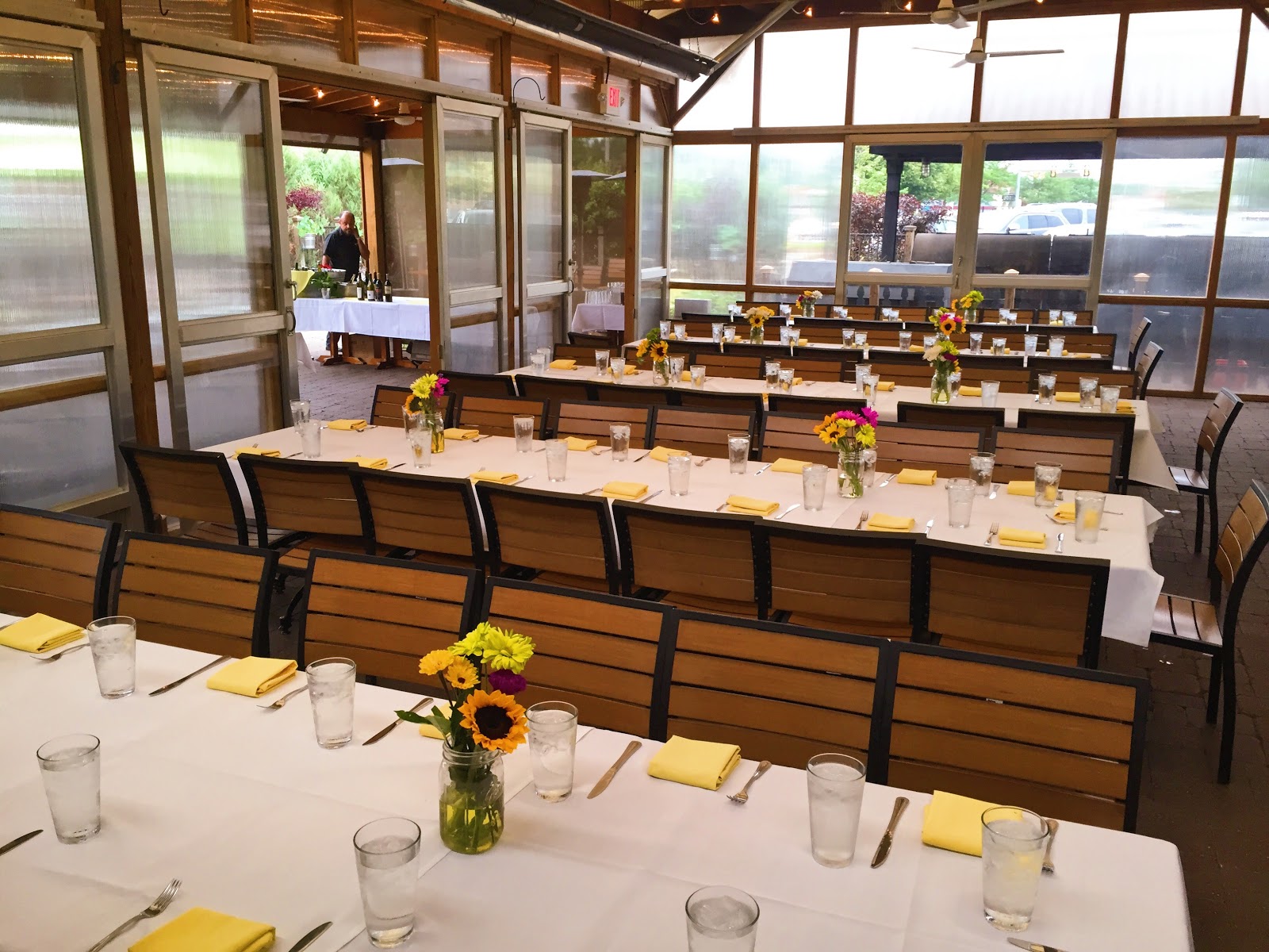 An enclosed patio space with ;png tables, set formally with tablecloths, colored napkins, and flowers.
