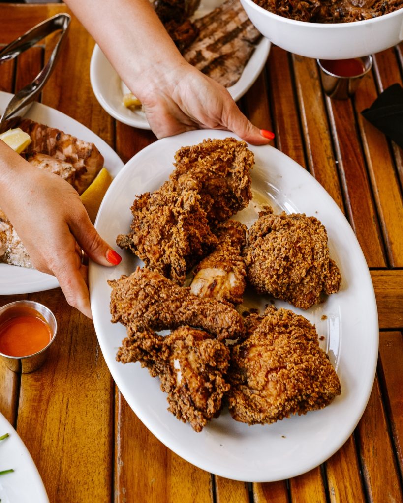 A pair of hands hold out a platter of crispy buttermilk fried chicken 