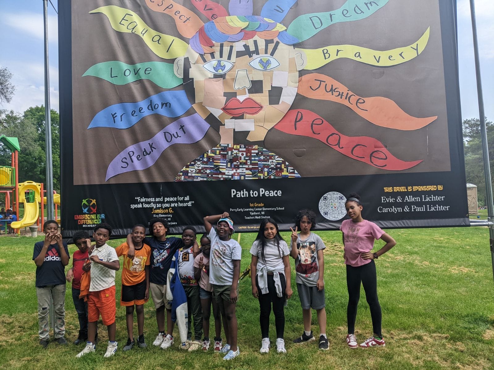 A group of children from diverse ethnic groups stand in front of a large, colorful art piece about diversity and inclusion.